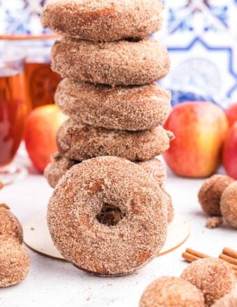 Cinnamon sugar apple cider donuts are placed in a stack on a white countertop.