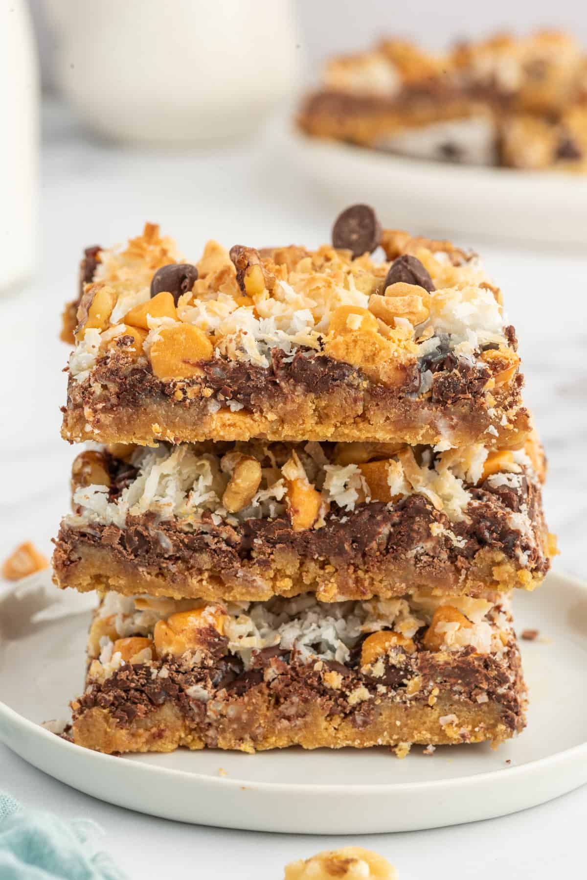 Three magic cookie bars are stacked on top of one another on a white plate.
