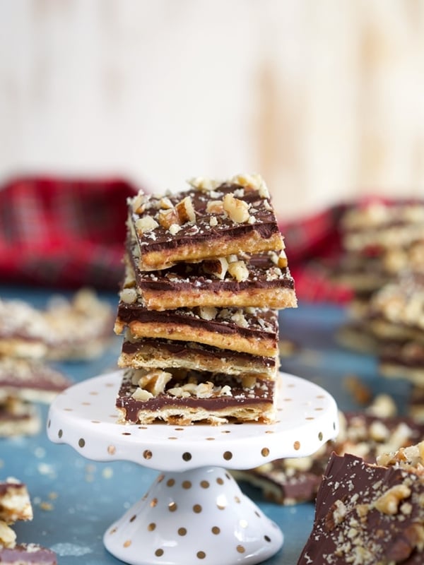 Saltine Cracker Toffee with nuts stacked on a white mini cake plate on a blue background.
