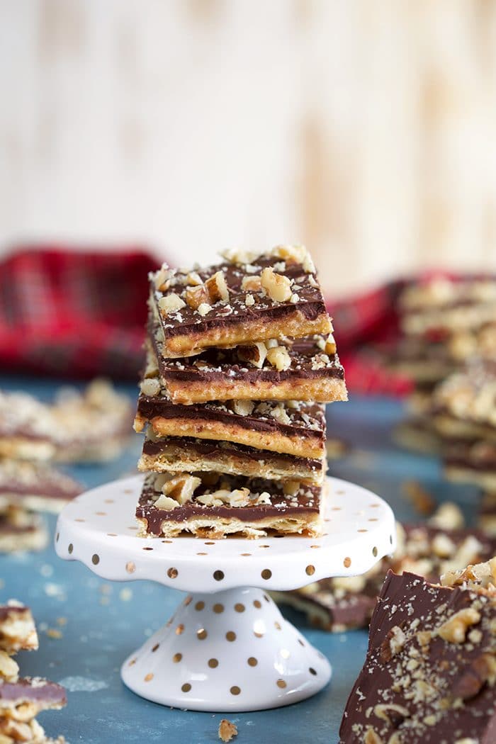 Saltine Cracker Toffee with nuts stacked on a white mini cake plate on a blue background.