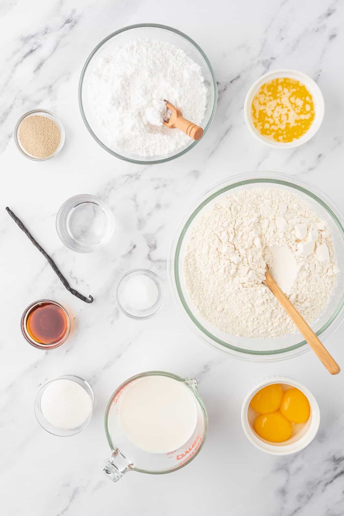 The ingredients for glazed vanilla donuts are spread out on a white surface.