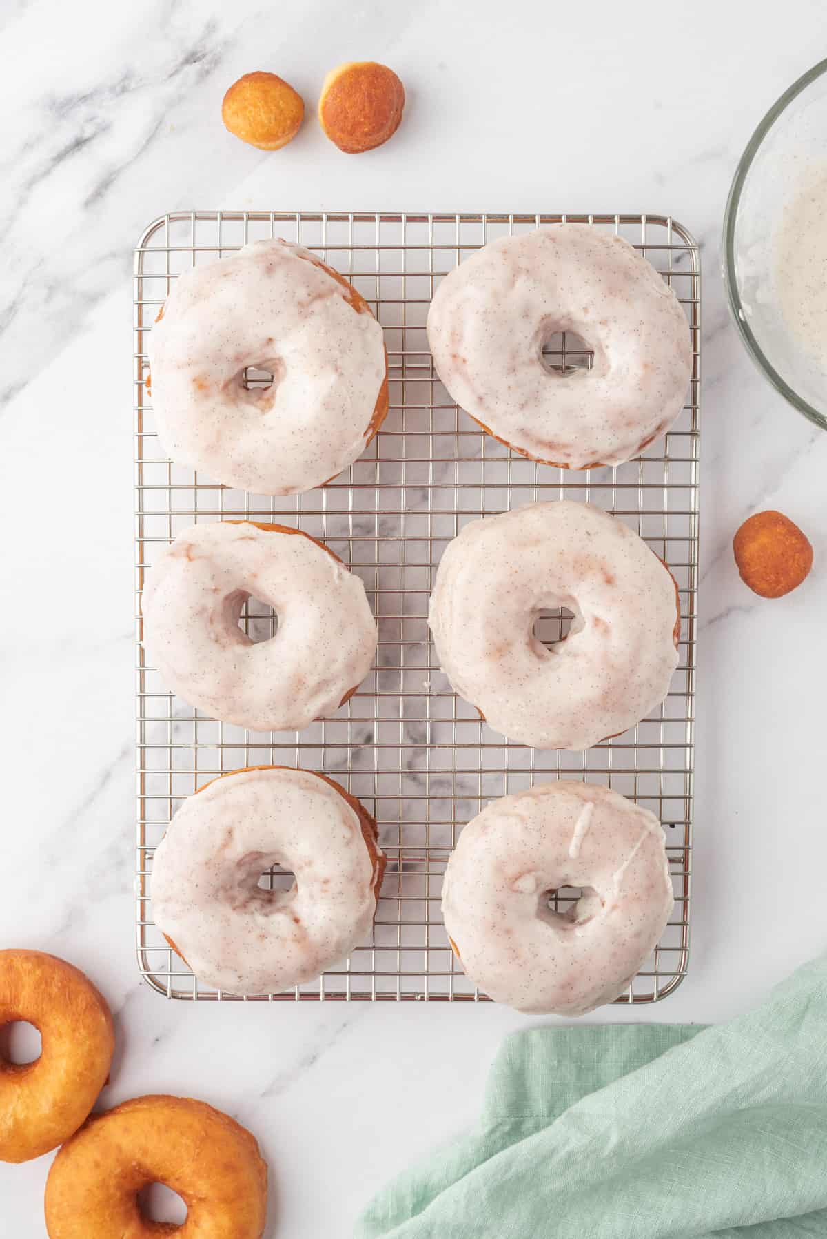Six donuts are placed on a wire cooling rack.