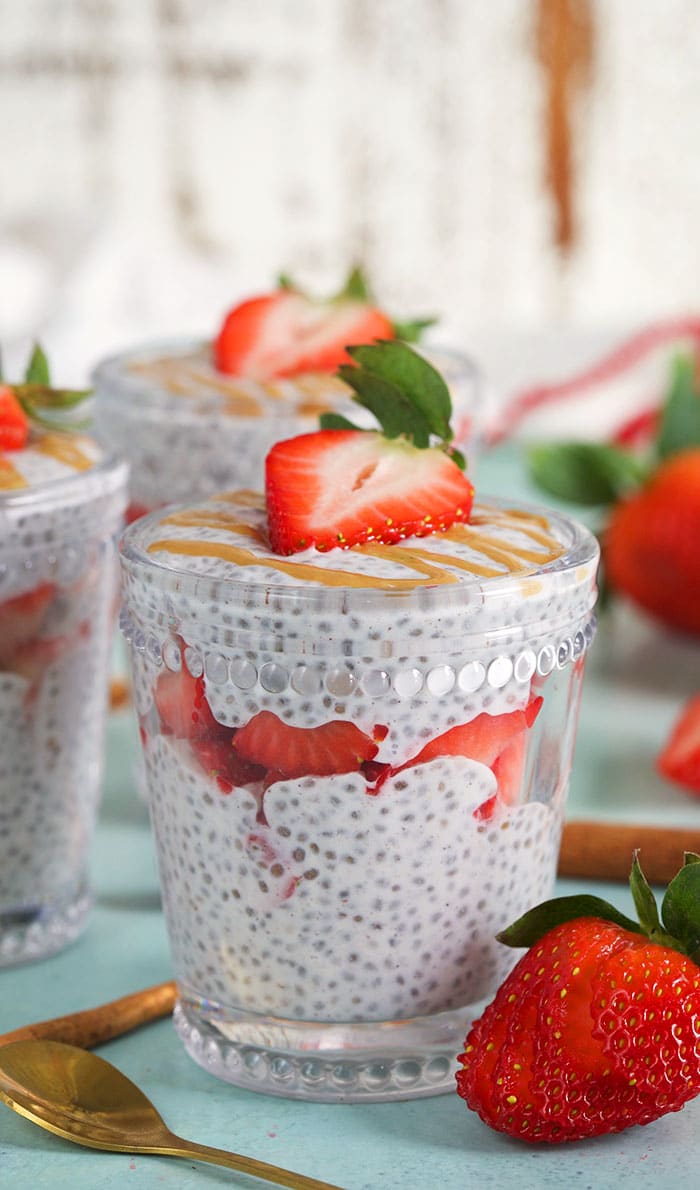 Three glasses with chia seed pudding layered with strawberries on a blue background.