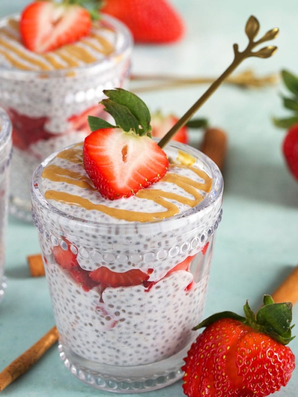 Chia Pudding layered in a glass with strawberries and a gold spoon.