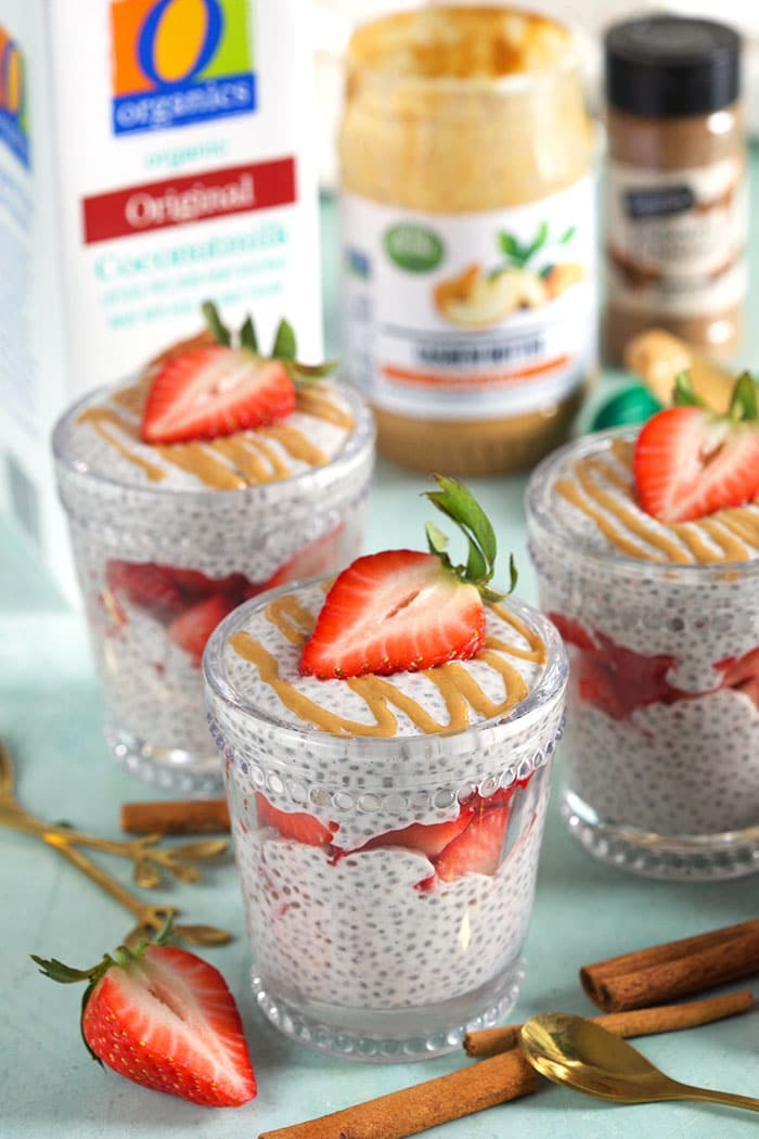 coconut chia pudding layered in a glass with strawberries with coconut milk, cashew butter and cinnamon in the background.