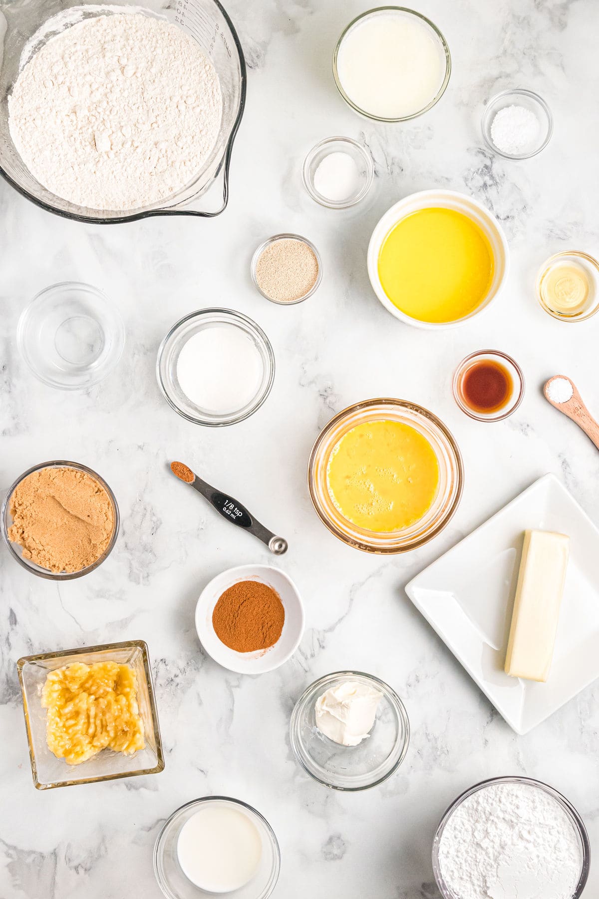 The ingredients for cinnamon rolls are spread out across a white countertop. 