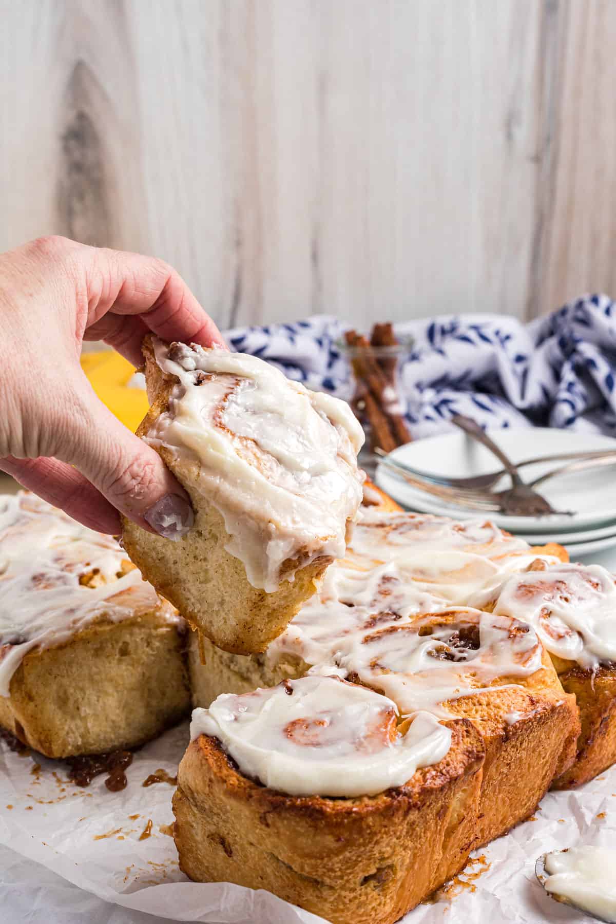 A single cinnamon roll is being lifted from the batch.