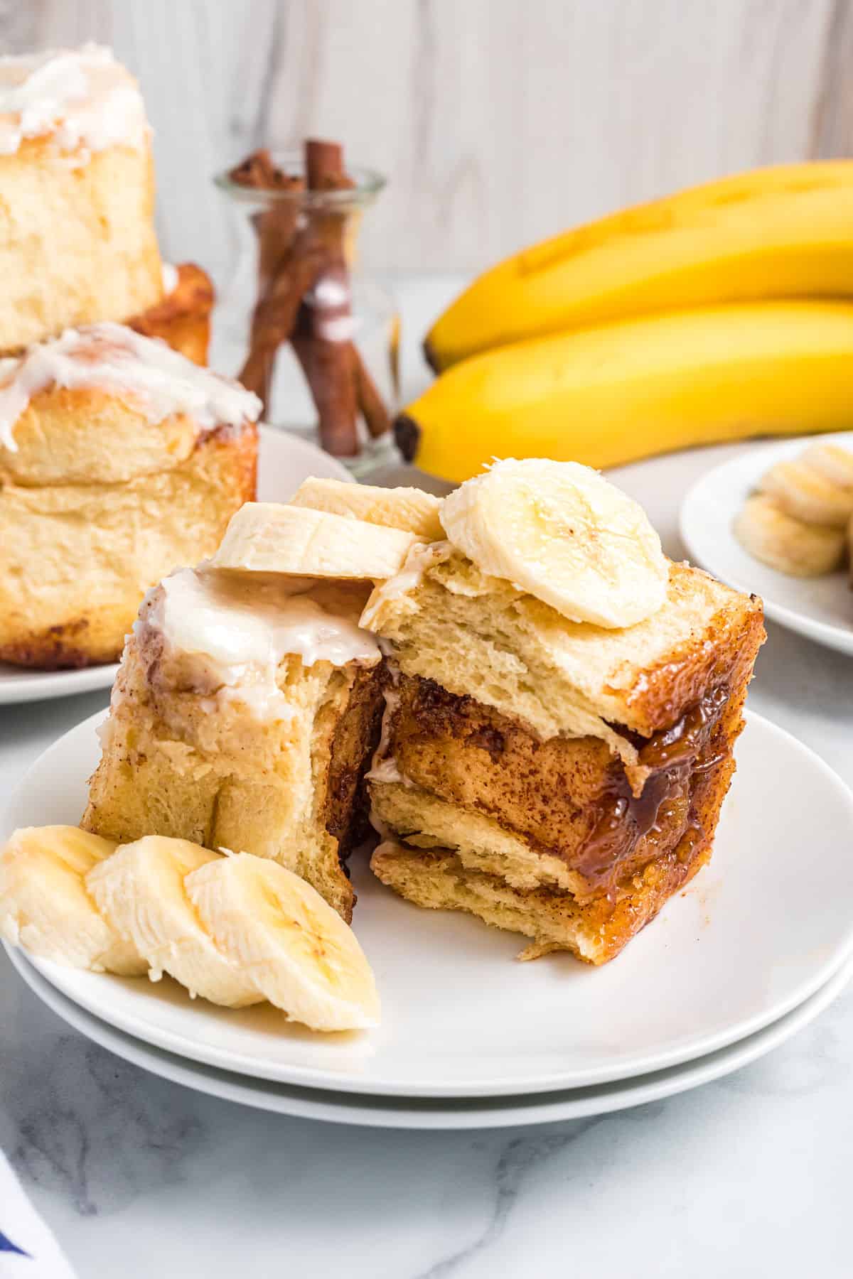 Banana slices are placed on top of and around a cinnamon roll on a white plate.
