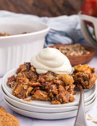 A dollop of whipped cream is on top of a serving of gingersnap apple crisp.