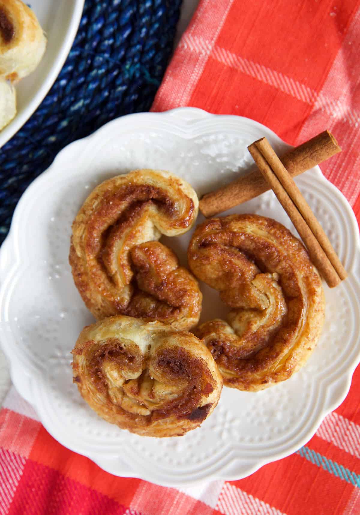Three palmiers are placed on a white plate with two small cinnamon sticks. 