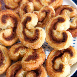 A round white plate of palmiers are presented on a blue placemat.