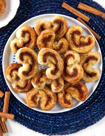 A round white plate of palmiers is presented on a blue placemat.