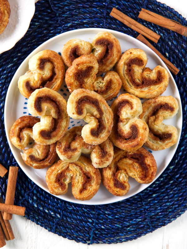 A round white plate of palmiers is presented on a blue placemat.