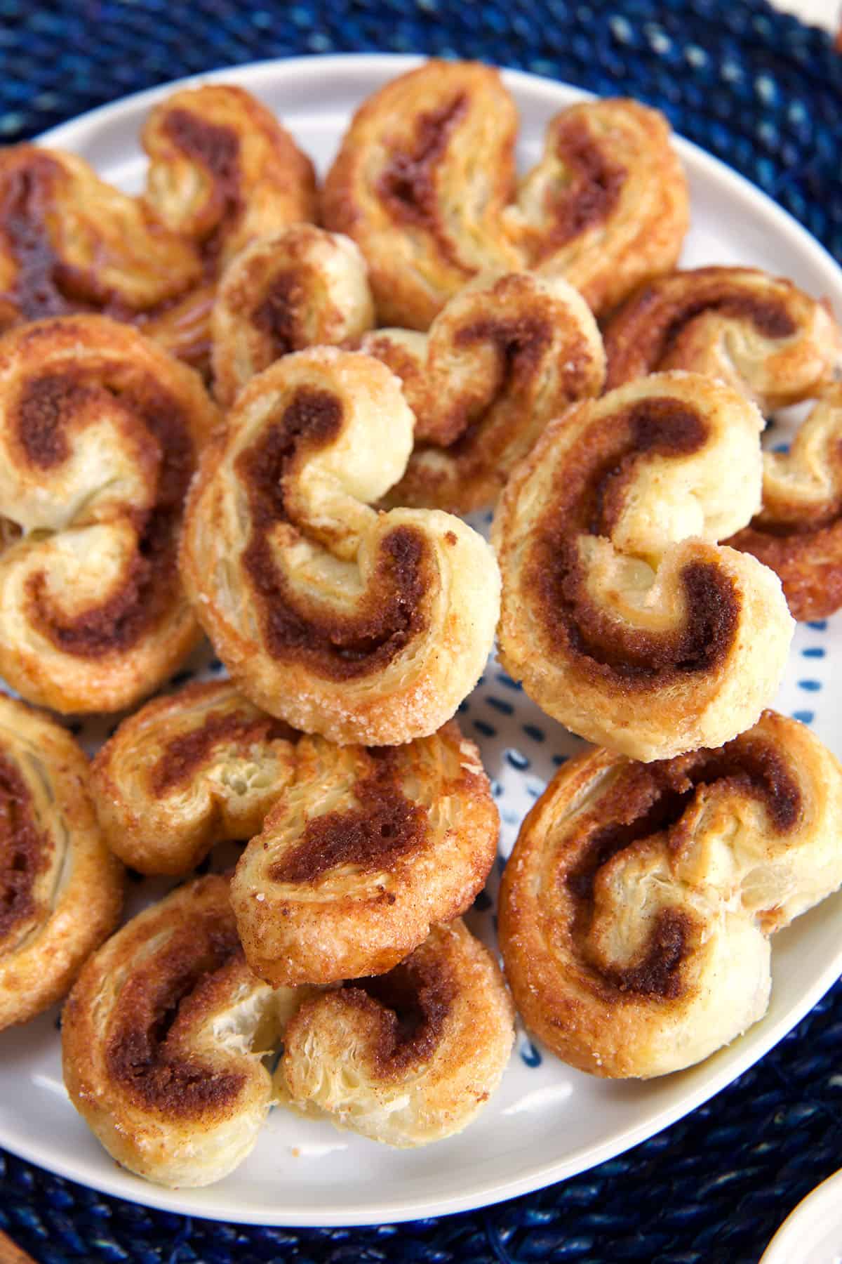 A round white plate of palmiers are presented on a blue placemat. 