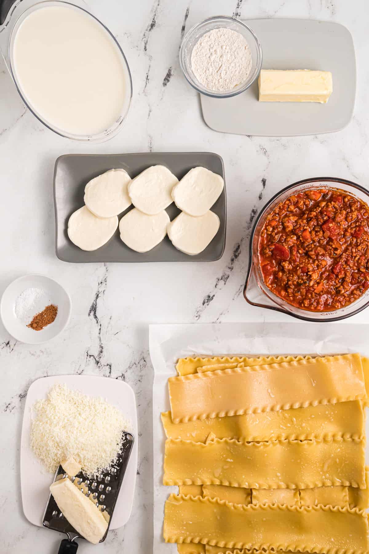 The ingredients for lasagna bolognese are placed on a white countertop.