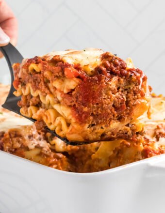 A slice of lasagna bolognese is being lifted from the baking dish.