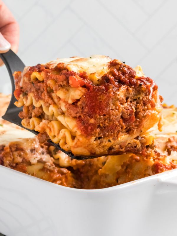 A slice of lasagna bolognese is being lifted from the baking dish.