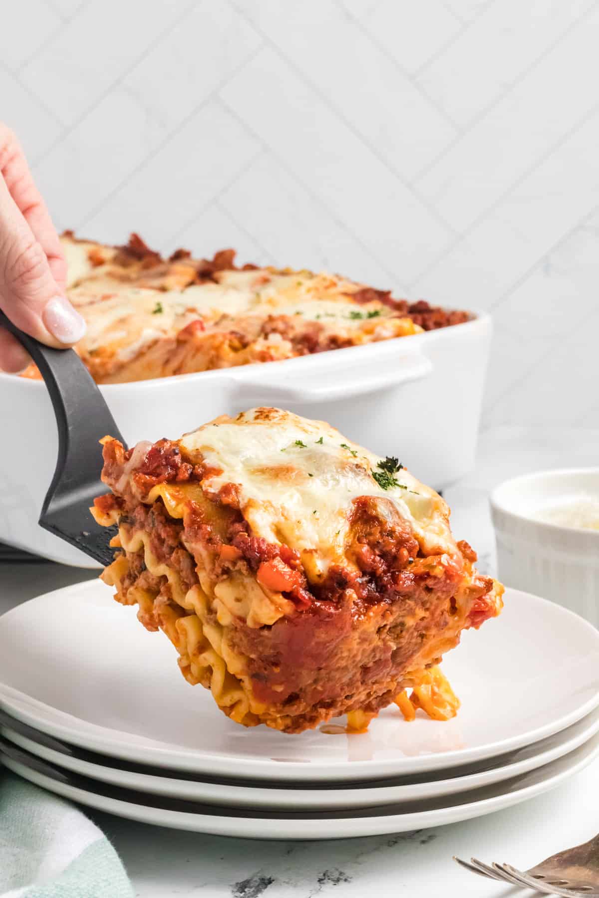 A slice of lasagna is being placed on a white plate.