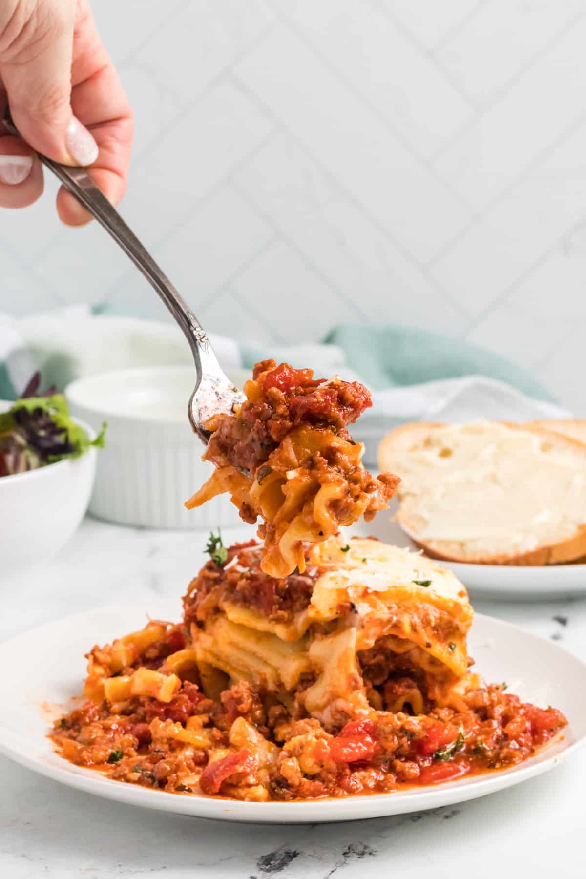 A fork is removing a bite of lasagna from a plated serving.