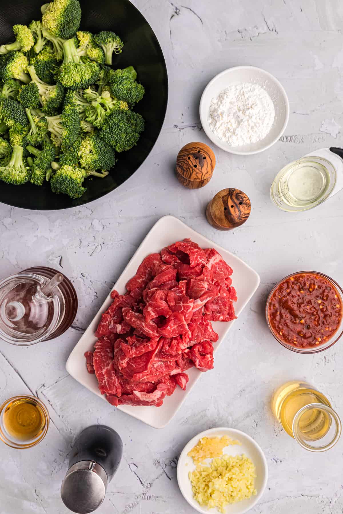 Ingredients for beef and broccoli are placed on a white countertop. 