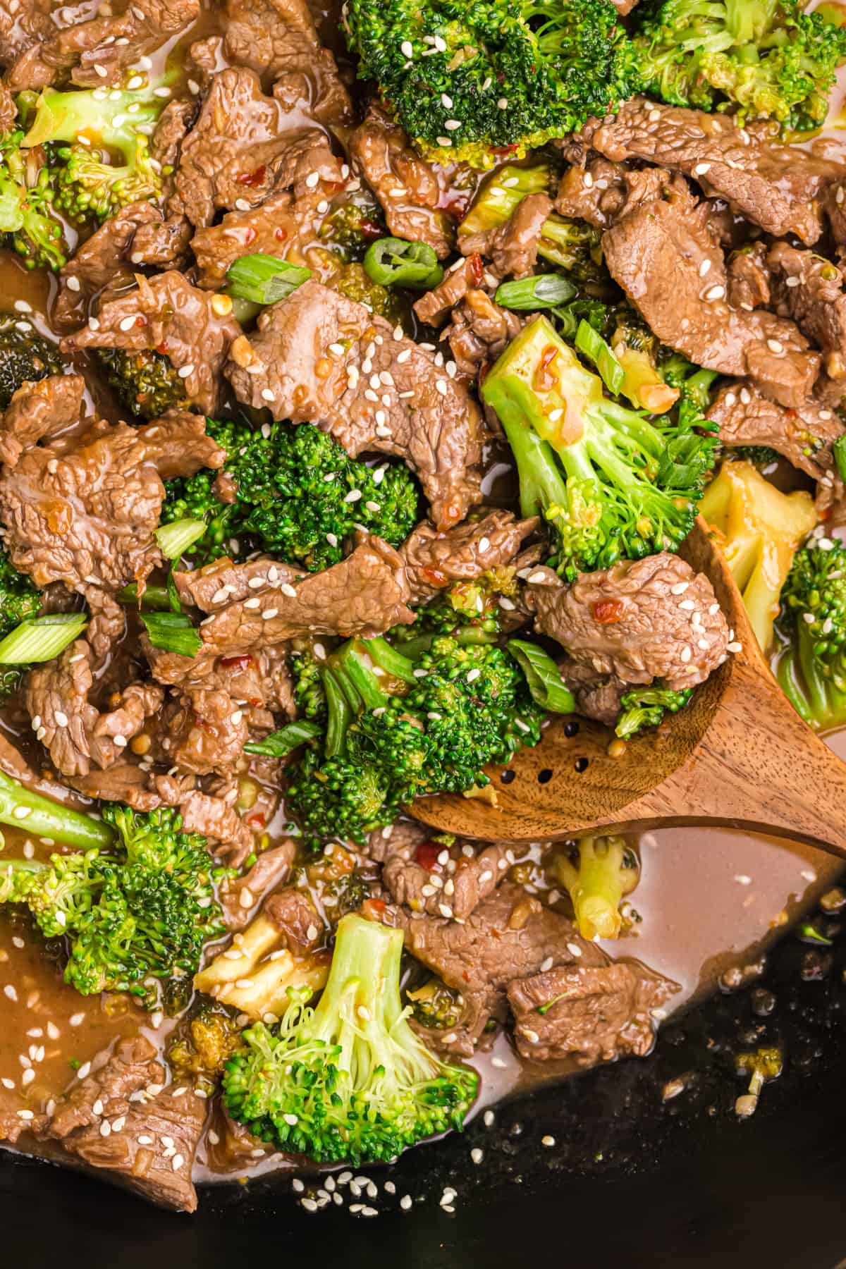 A wooden stirring spoon is placed in a skillet filled with beef and broccoli.