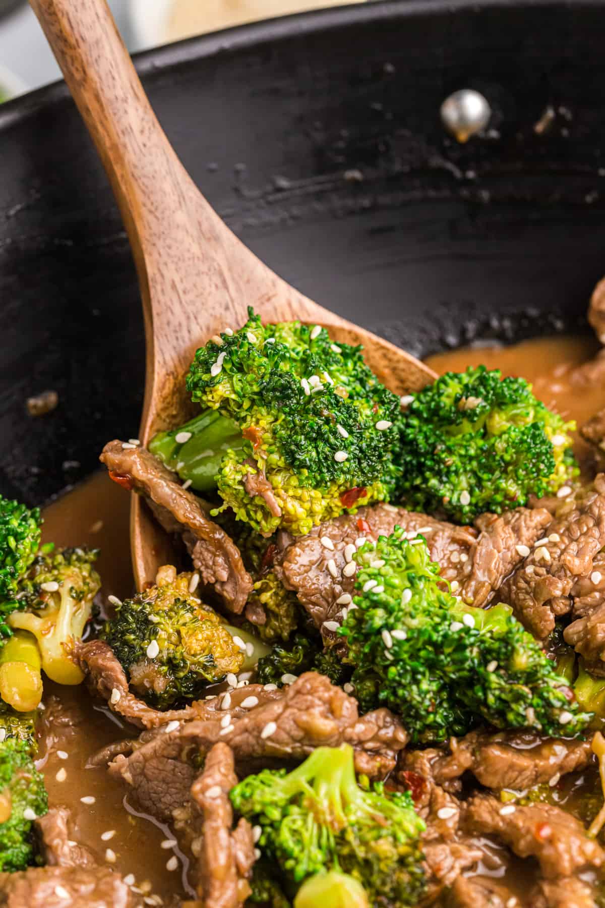 A wooden spoon is lifting a small portion of beef and brococli from the pan.