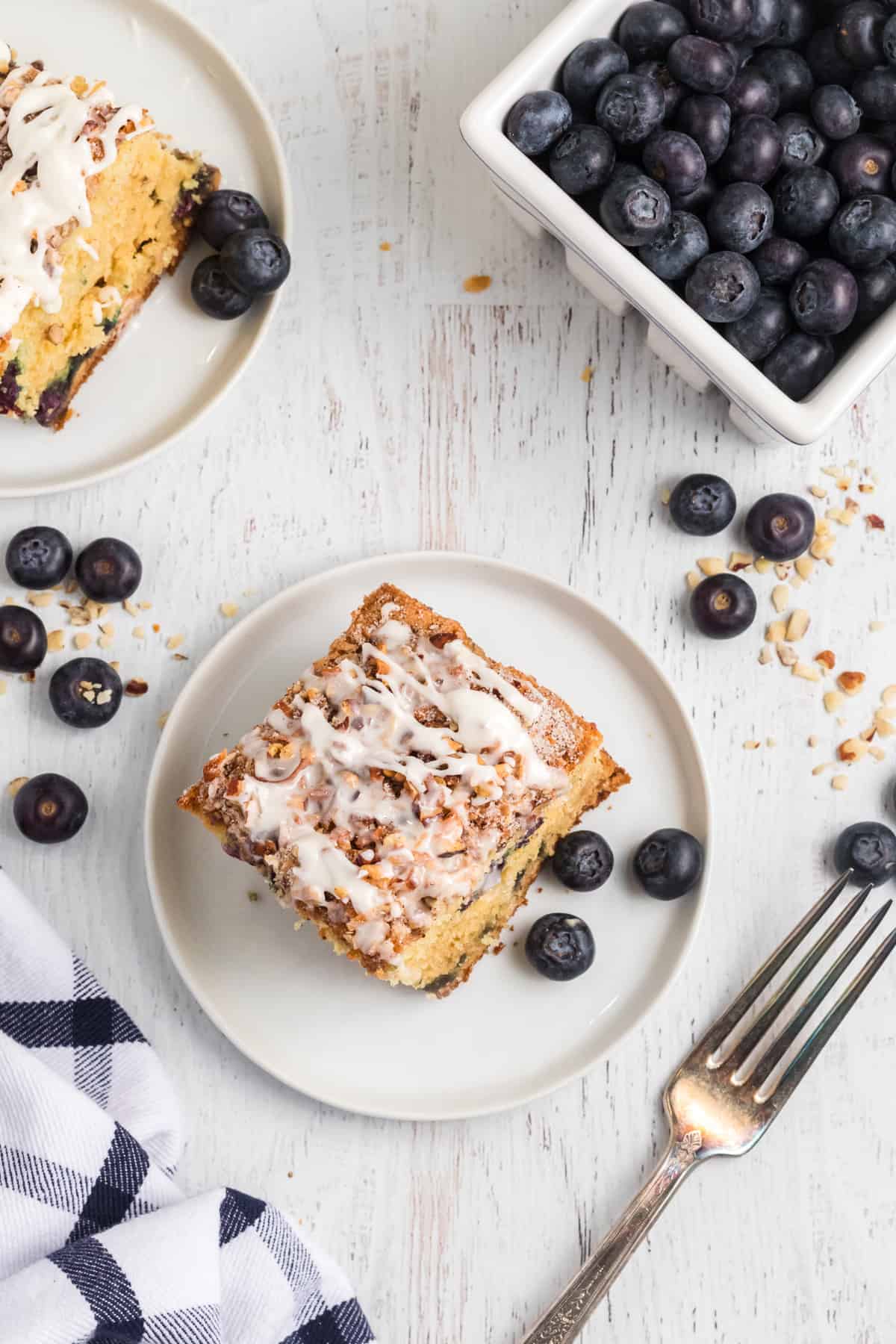 Two plates with servings of cake are placed next to a container of fresh blueberries.