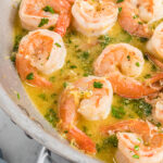Shrimp is being cooked in a buttery sauce in a silver skillet.