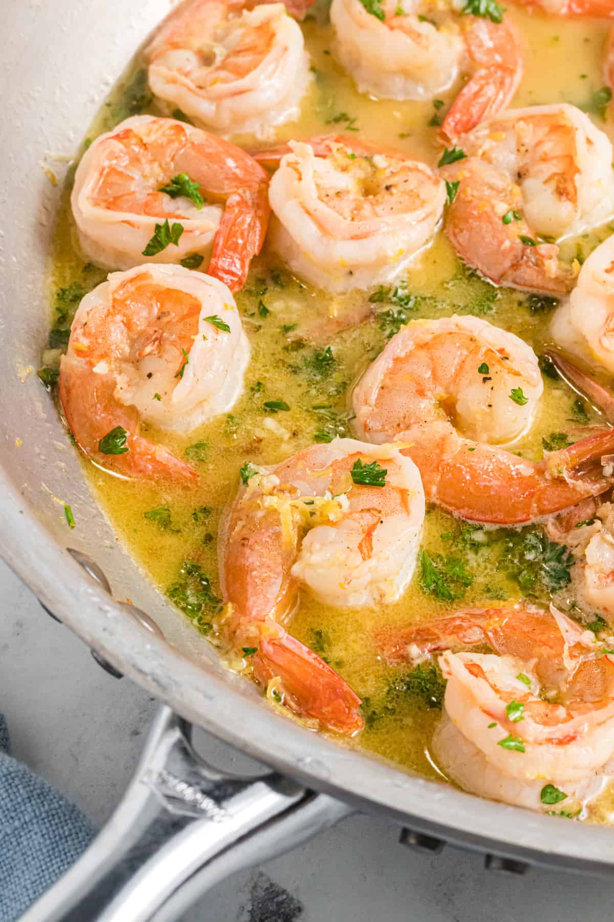 Shrimp is being cooked in a buttery sauce in a silver skillet.
