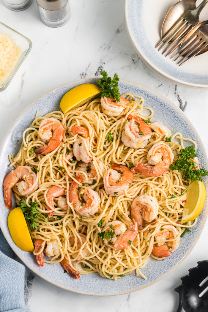 A large white plate is presented with noodles, shrimp, and lemon slices.