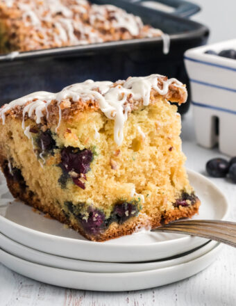 A large slice of blueberry coffee cake is placed on a stack of white plates.