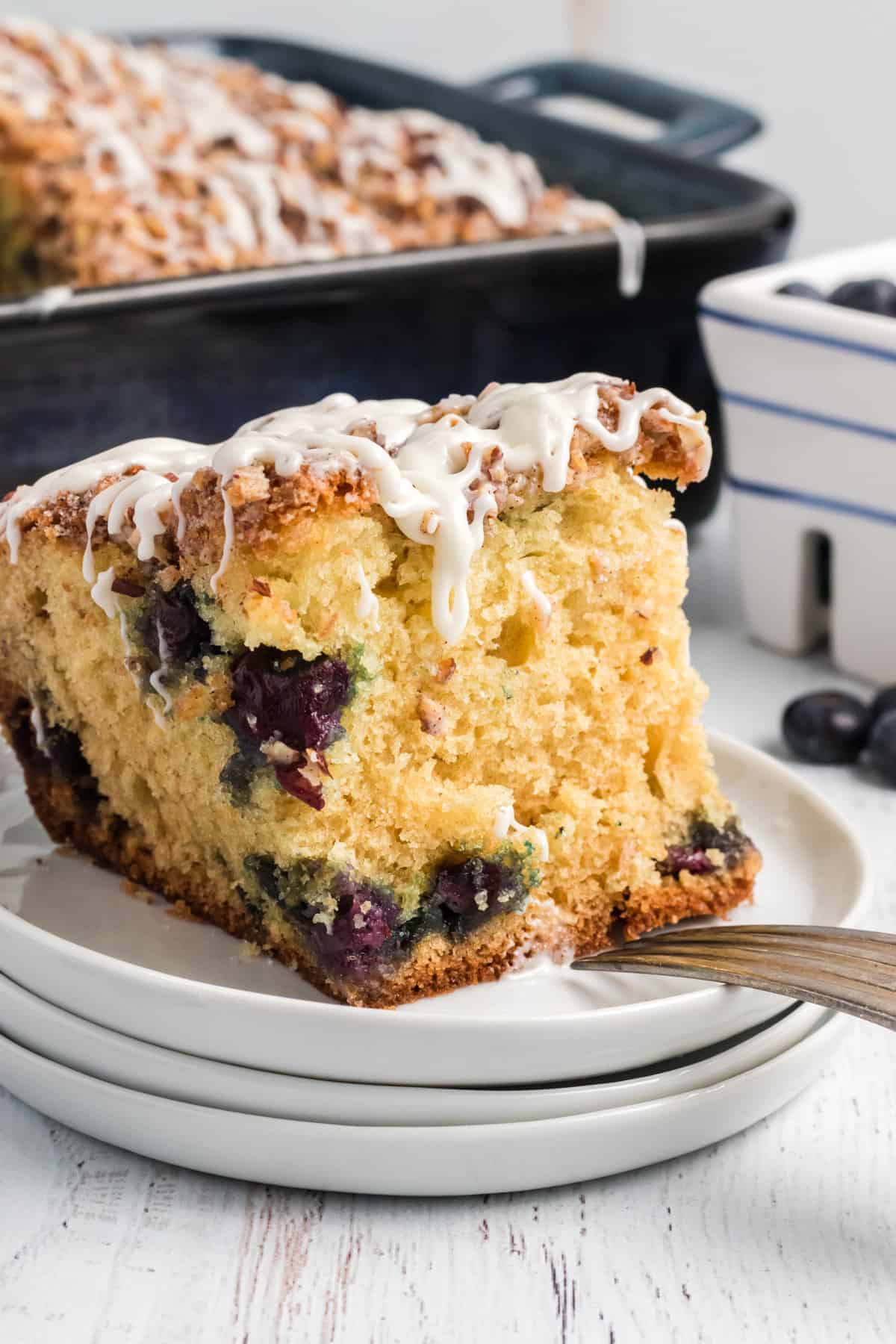 A large slice of blueberry coffee cake is placed on a stack of white plates.
