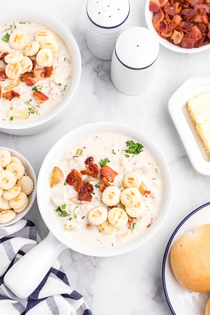 Two bowls of clam chowder are presented on a white countertop. 