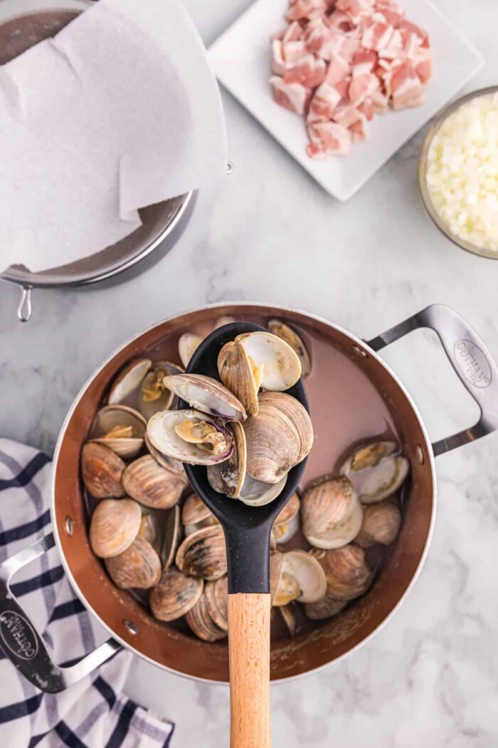 Steamed clams are being removed with a large spoon.