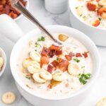 A bowl of clam chowder is topped with fried bacon bits.