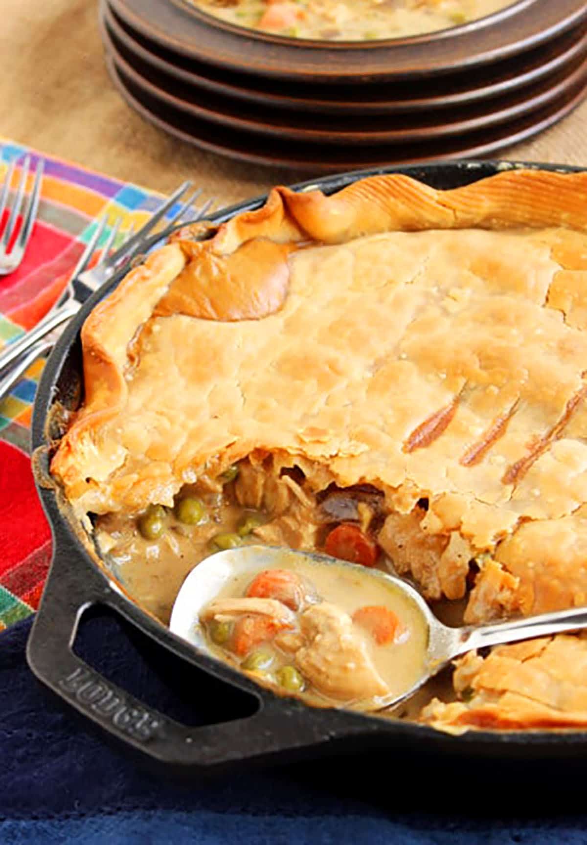 Chicken pot pie in a skillet with a spoon scooping it out and a plate in the background.