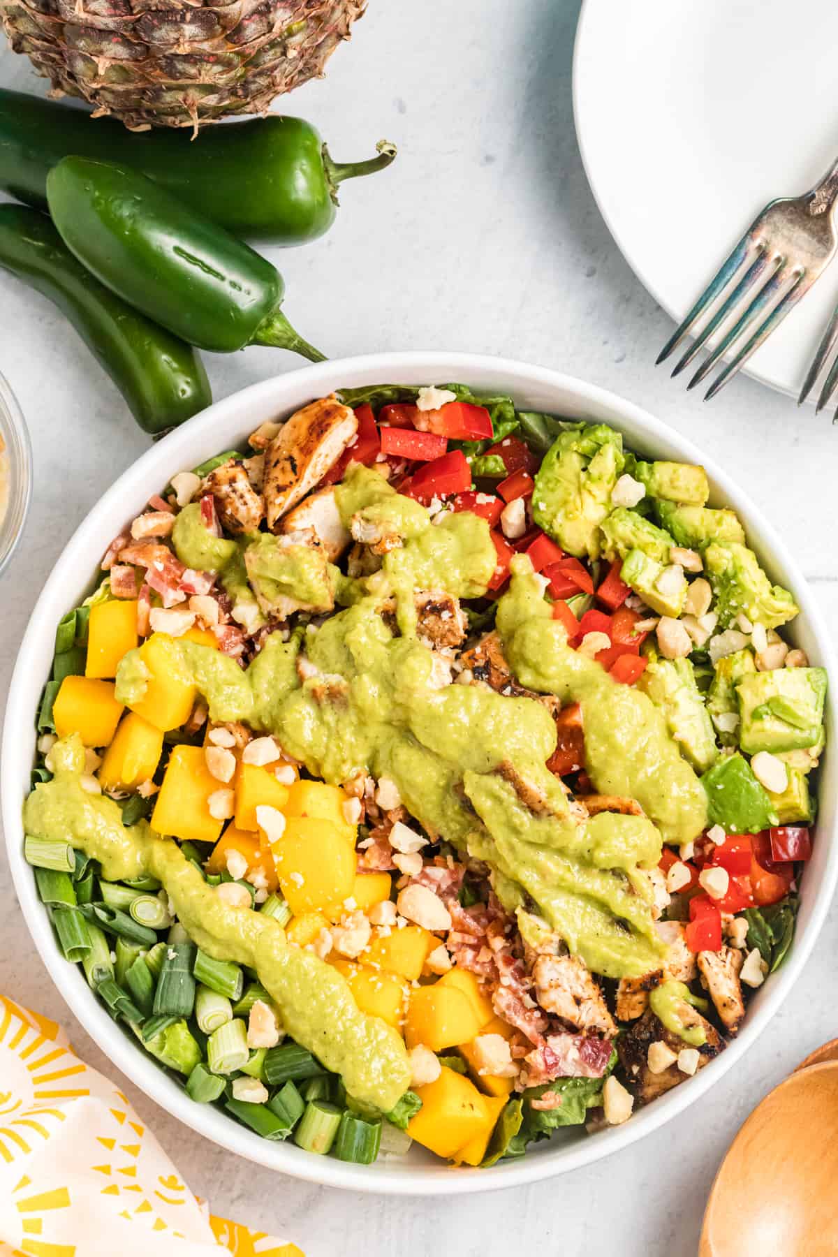 A bowl of Caribbean cobb salad is placed next to jalapenos on a white surface.
