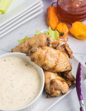 Several wings are placed on a white plate next to a bowl of white dipping sauce.