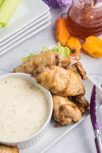 Several wings are placed on a white plate next to a bowl of white dipping sauce.