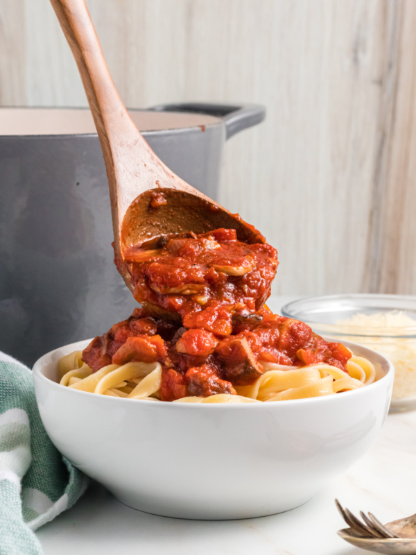 Mushroom bolognese is being placed on top of a serving of cooked pasta.
