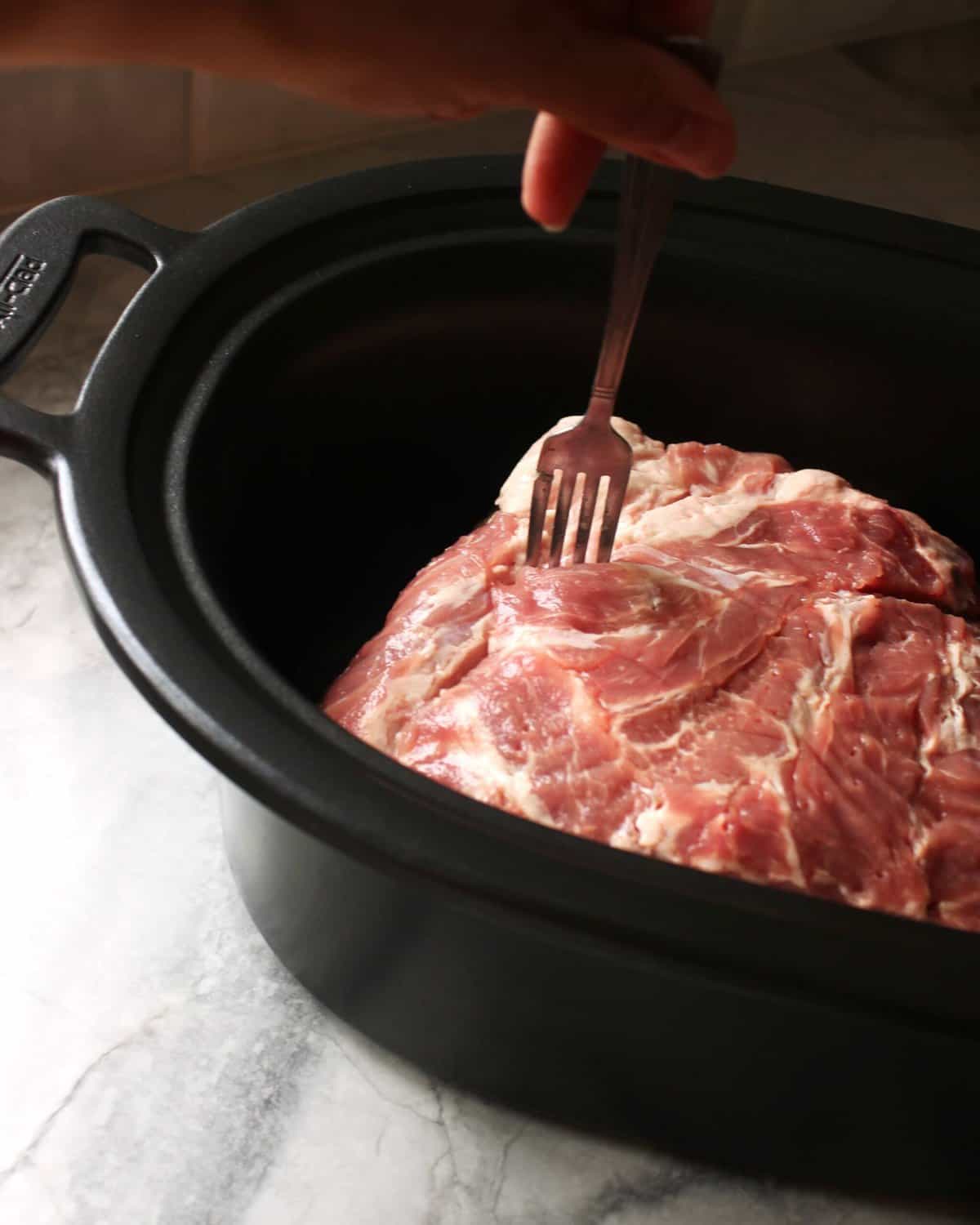 Pork being pierced with a fork in a slow cooker for Kalua Pork