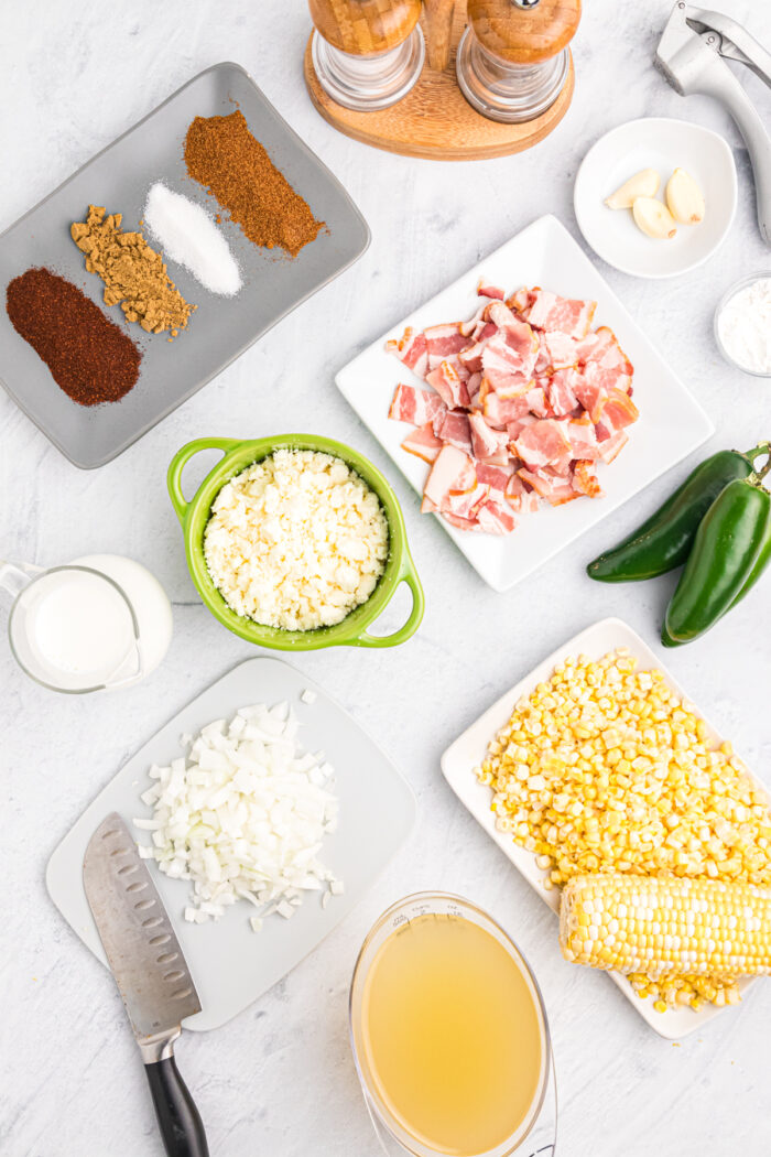 The ingredients for corn chowder are spread out across a white surface.