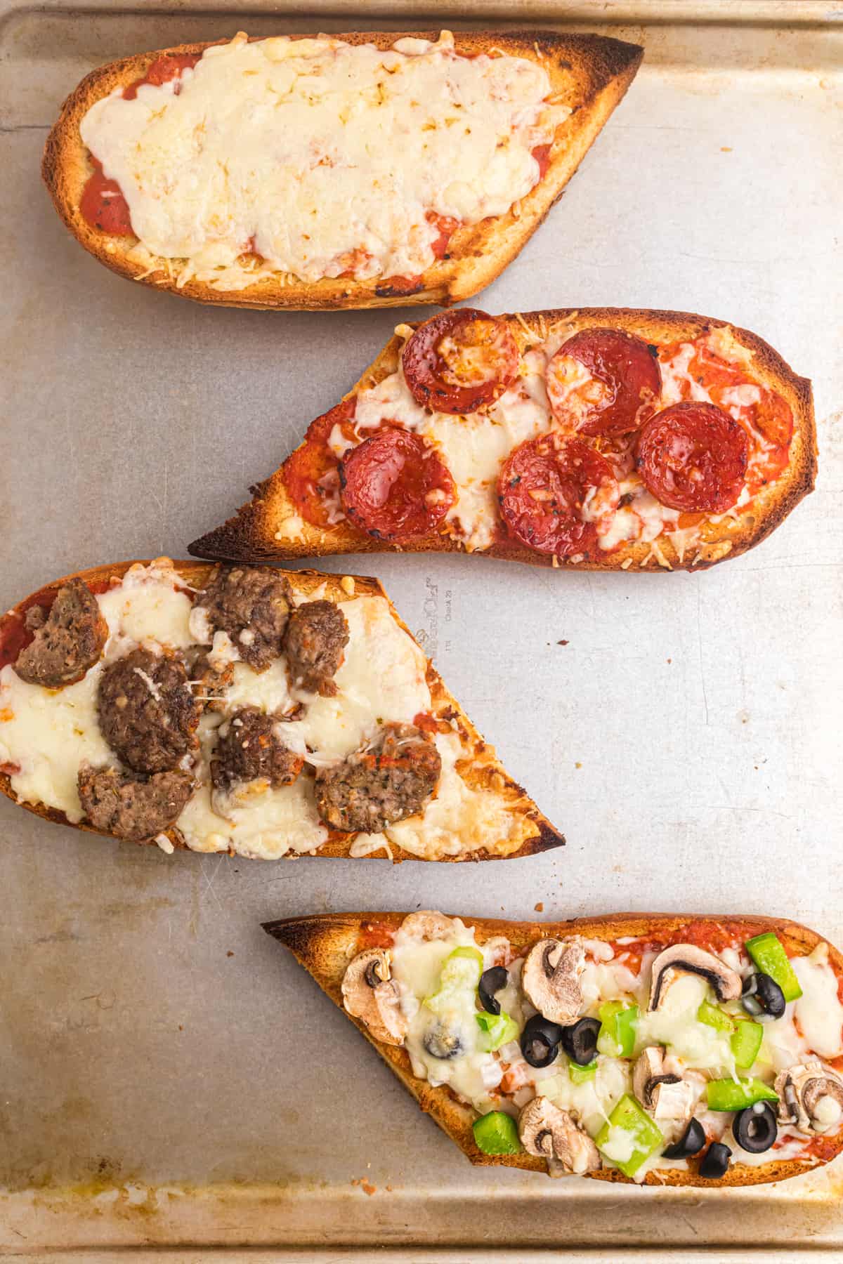 Four slices of cooked french bread pizza are placed on a baking sheet.