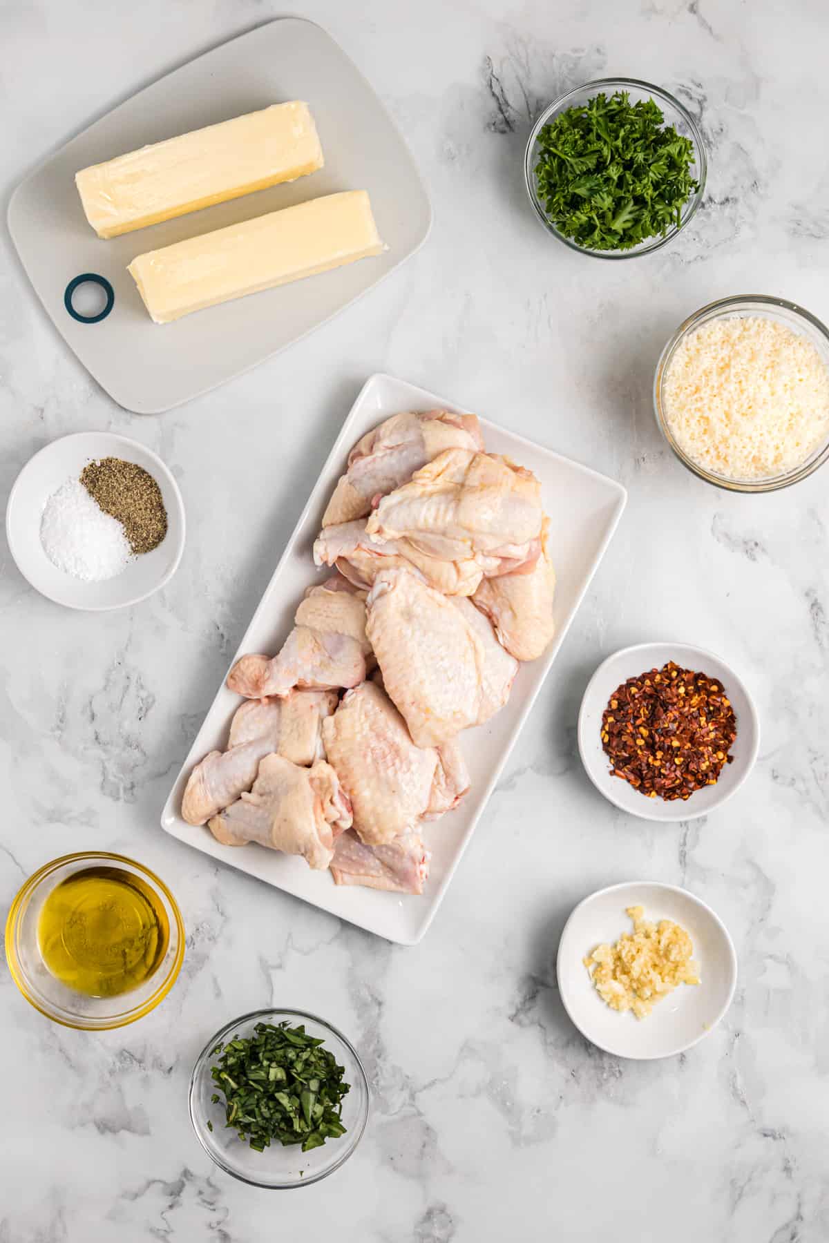 The ingredients for the chicken wings are spread out across a marble countertop. 