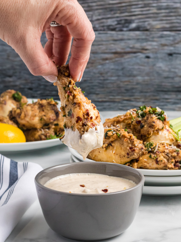 A chicken wing is being dipped into a container of white sauce.