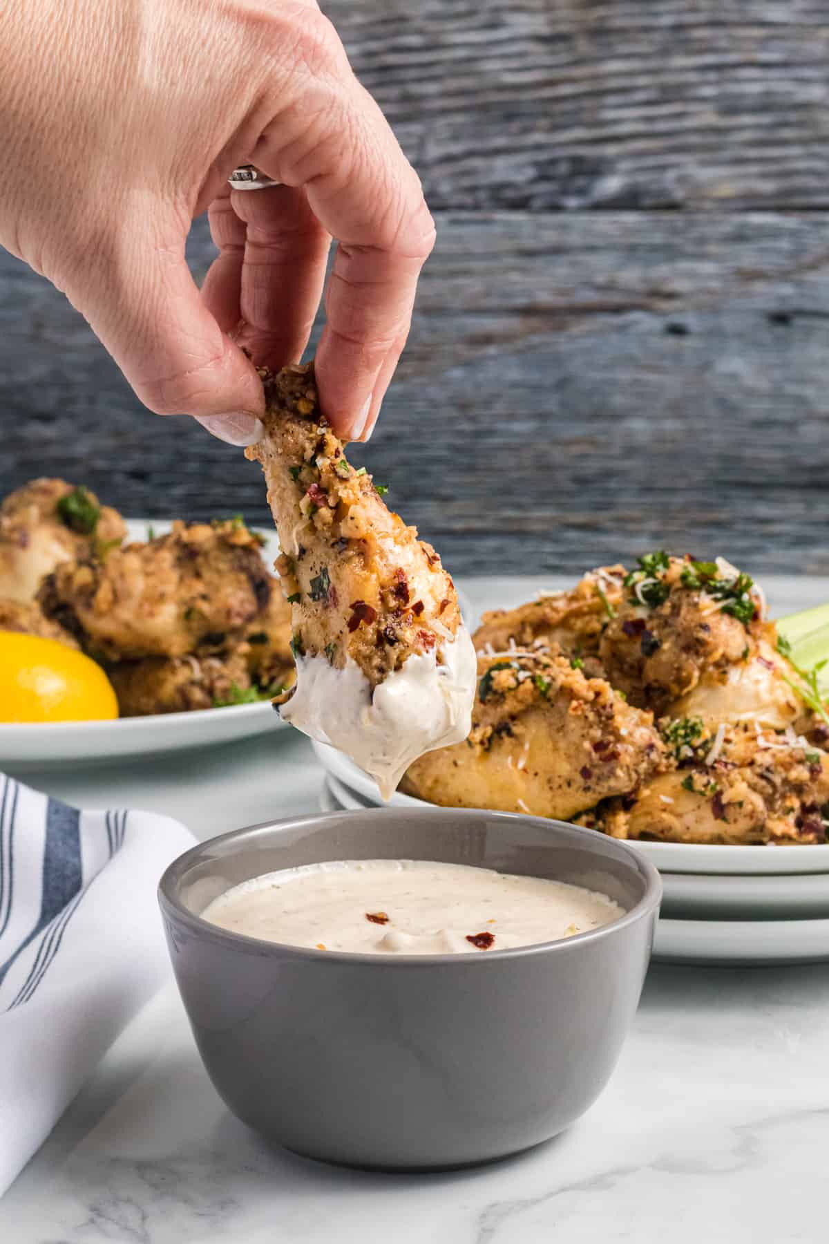 A chicken wing is being dipped into a container of white sauce.