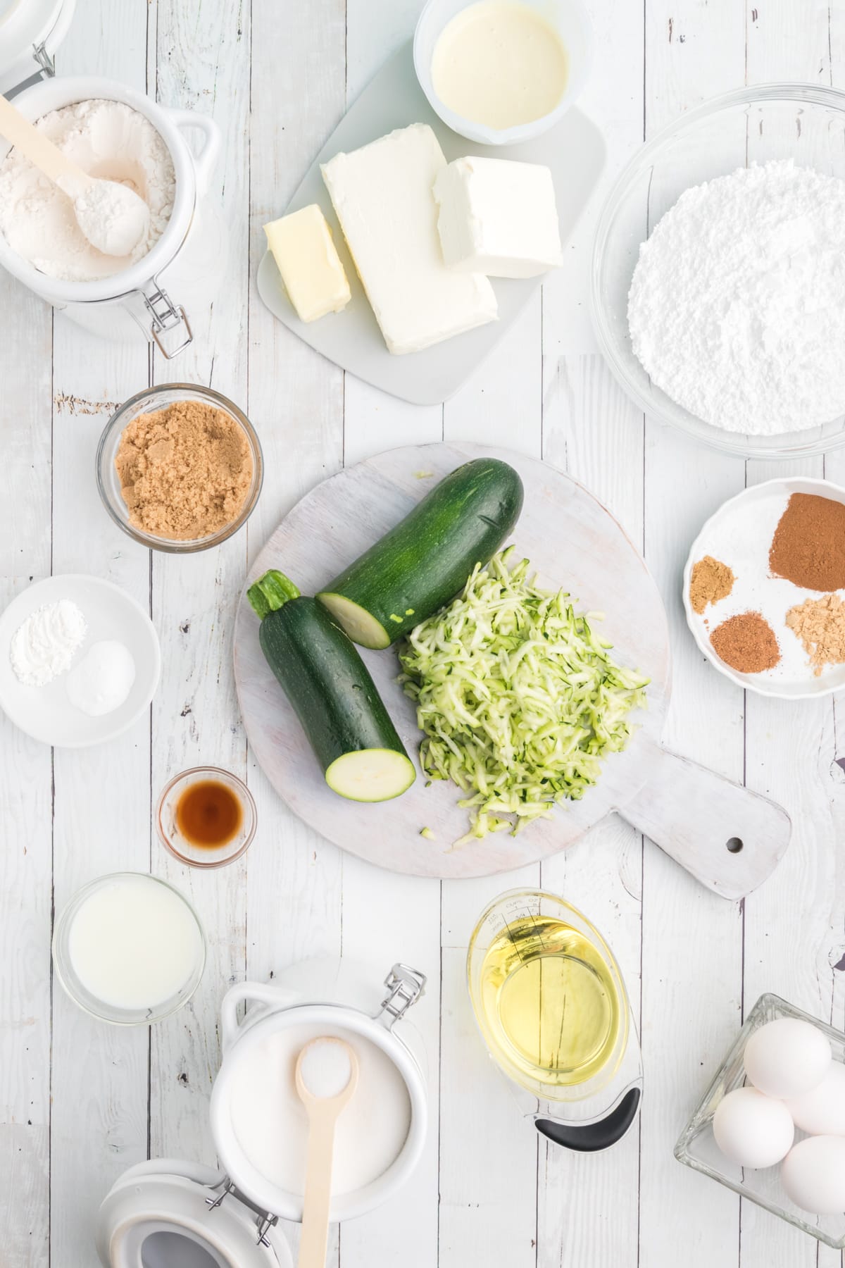 The ingredients for zucchini cake are spread out across a white surface.