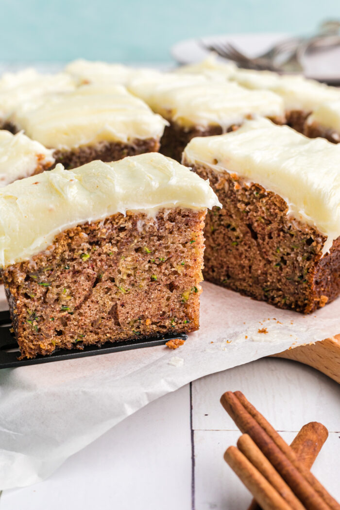 Several frosted pieces of zucchini cake are placed on a white serving platter.