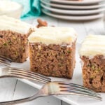 Several slices of zucchini cake are presented next to two forks on a white plate.