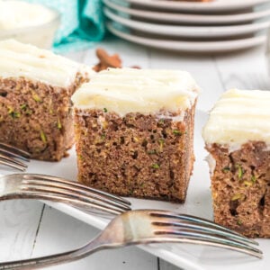 Several slices of zucchini cake are presented next to two forks on a white plate.